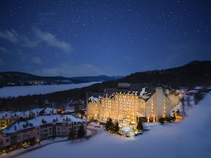 Un hôtel enneigé, avec un grand bâtiment, une piscine et une vue sur un paysage hivernal sous un ciel étoilé.