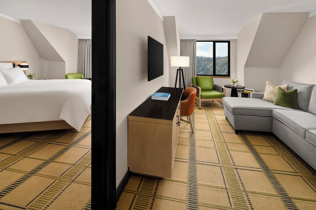 A hotel room with a bed, desk, chair, sofa, and a view of the outdoors.