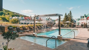 A pool area with lounge chairs, a water feature, and a view of buildings in the background. - Fairmont Tremblant (Mont-Tremblant)