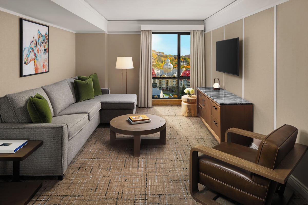 A hotel room with a sofa, armchair, round coffee table, and a TV on the wall.