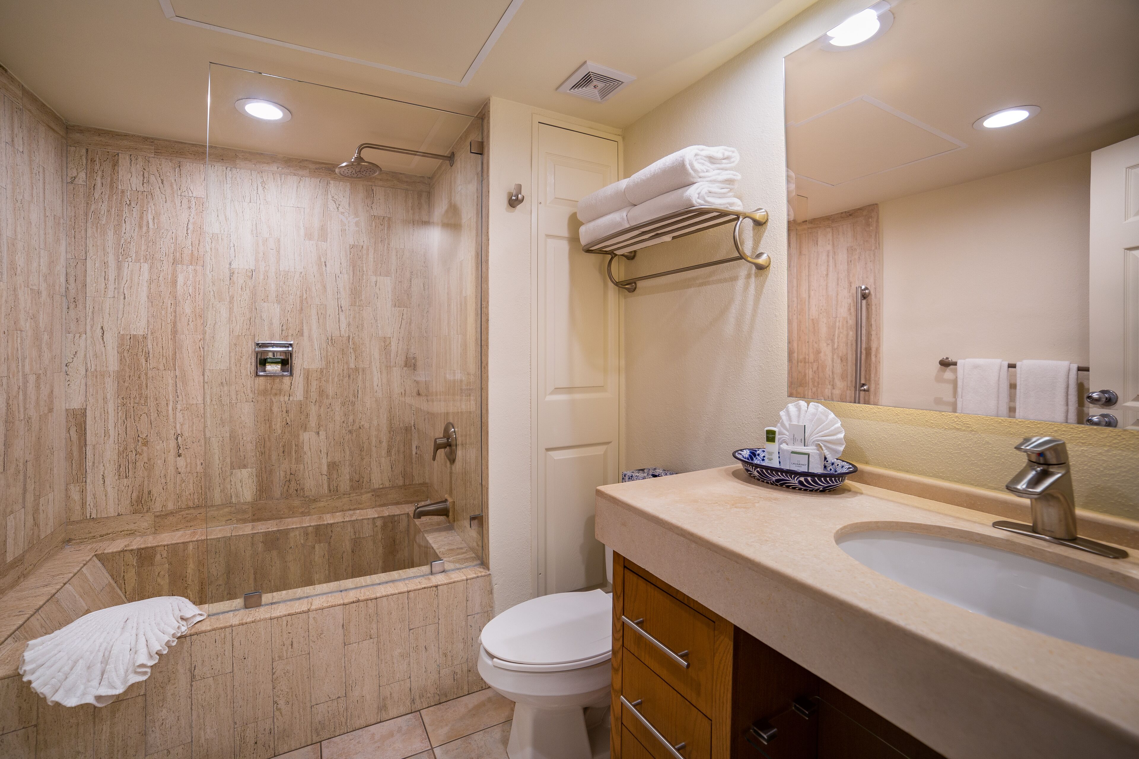 Un baño moderno con ducha de mármol, inodoro, lavamanos con espejo y toallero.