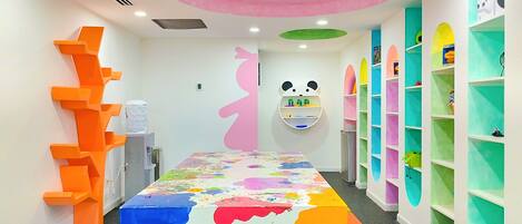 A brightly colored room with a large table covered in paint, a panda-themed shelf, and colorful shelves along the walls.