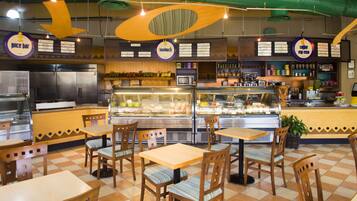 L’intérieur d’un restaurant avec un sol à carreaux, des tables et des chaises en bois, un comptoir avec une vitrine et des enseignes suspendues.