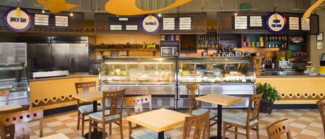 A restaurant interior with a checkered floor, wooden tables and chairs, a counter with a display case, and hanging signs.