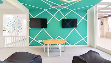 Habitación moderna con paredes color turquesa, dos pantallas negras montadas en la pared, una mesa de madera y dos sillones de felpa negros.