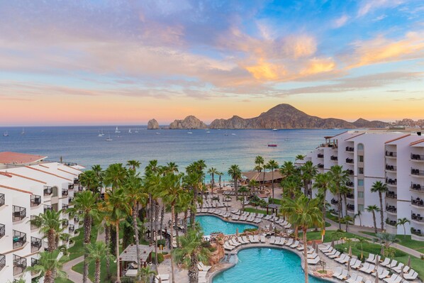 Relax by the resort's large, curved pool surrounded by palm trees and lounge chairs, with sailboats visible in the distance.