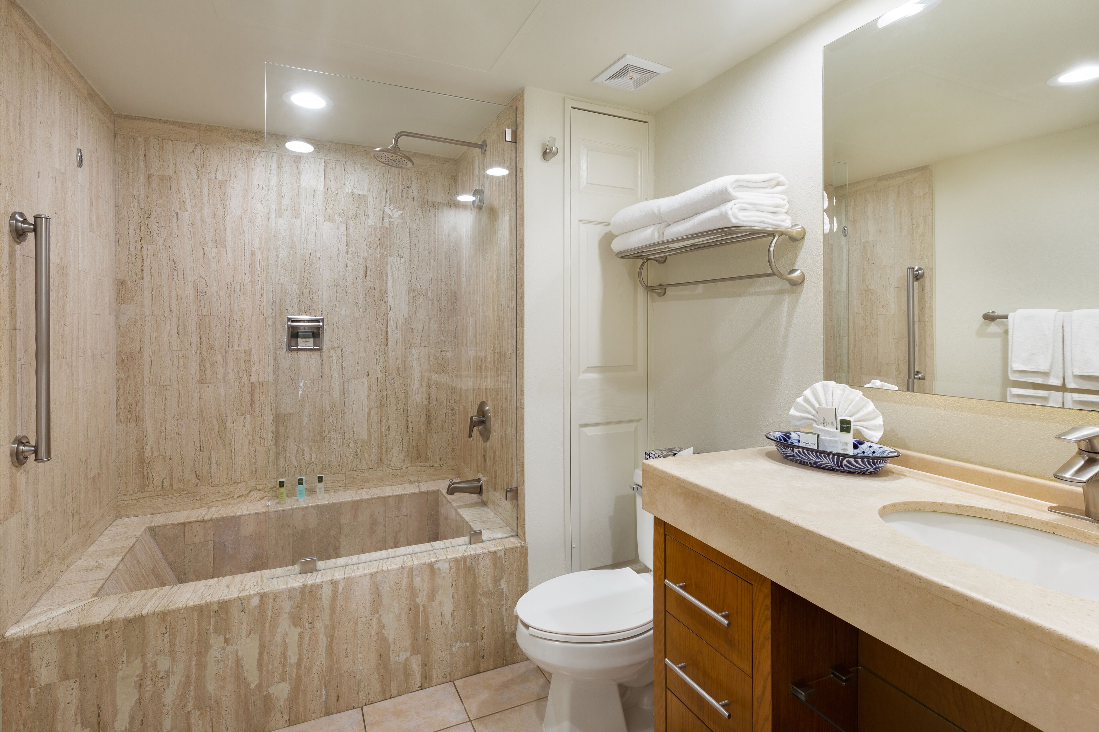 A modern bathroom with a large bathtub, a toilet, and a sink with a mirror.