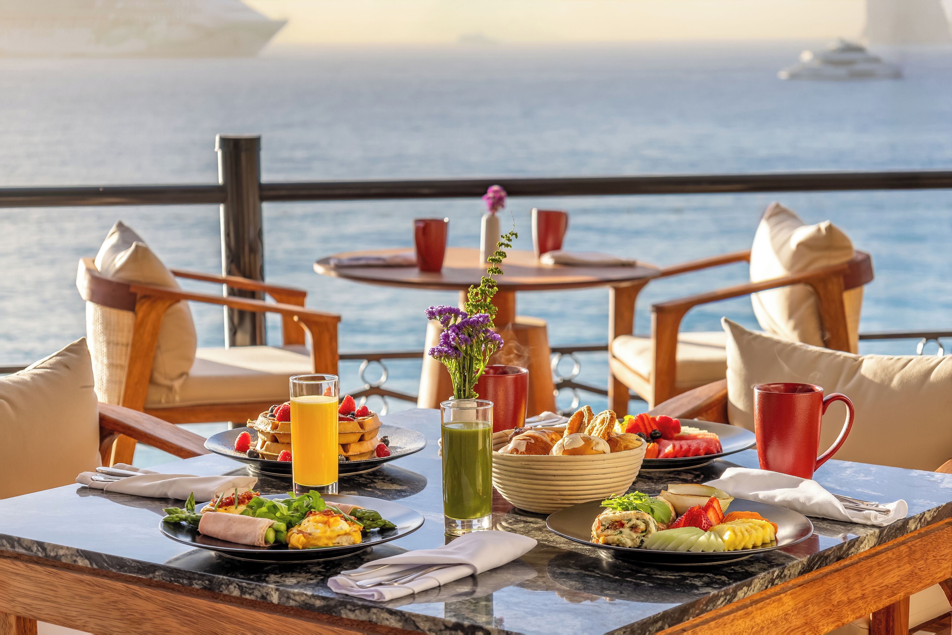 Een eettafel met ontbijtartikelen, een vaas met bloemen en uitzicht op de zee.