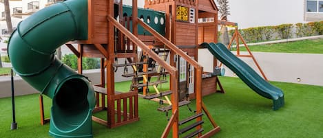 Un'area giochi con uno scivolo, una struttura per arrampicarsi e un tunnel verde.
