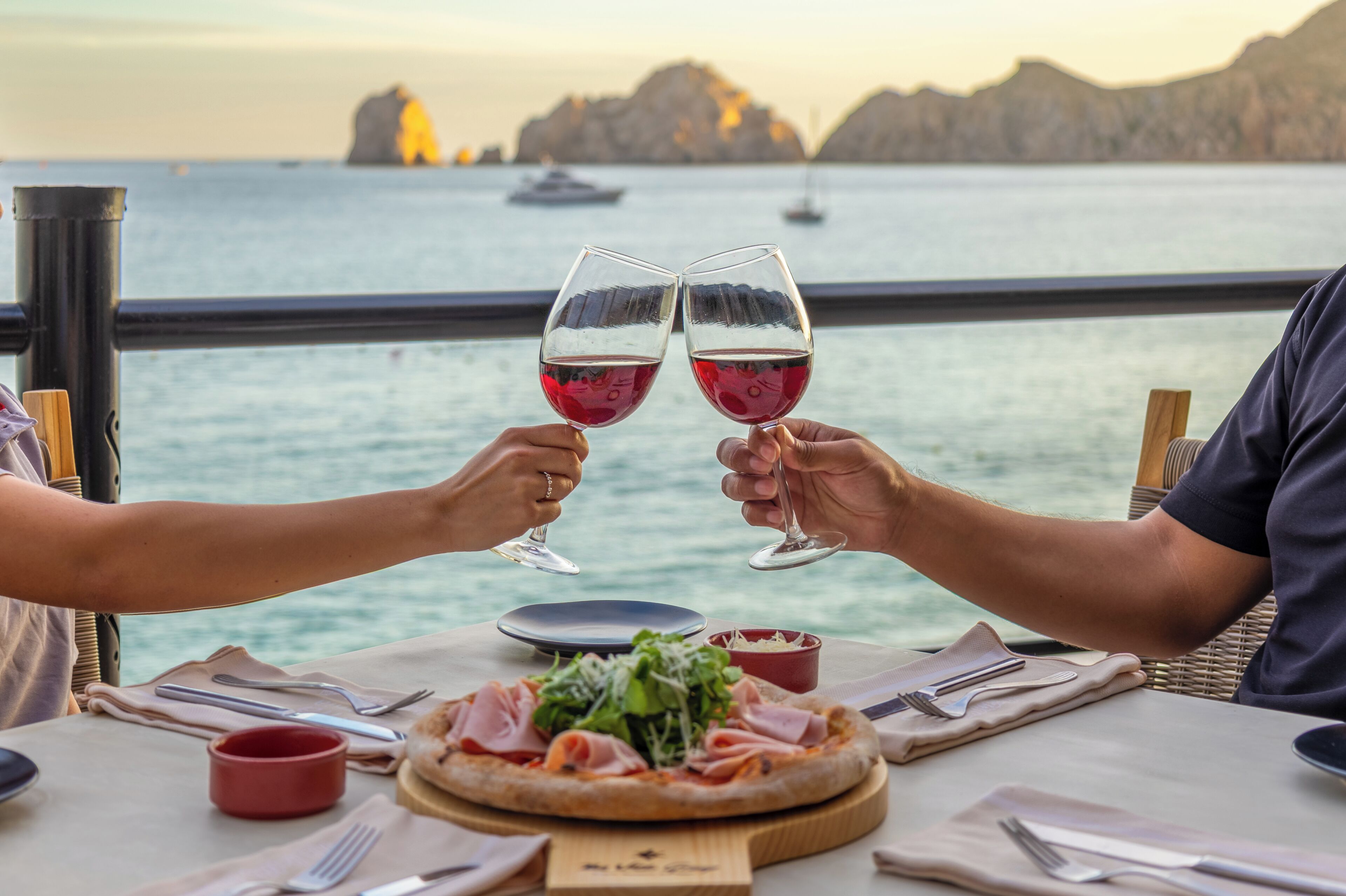 Un tavolo con pizza, bicchieri di vino e vista sul mare.