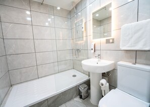 A modern bathroom with a bathtub, sink, toilet, and a trash bin. - Rushmore Hotel (London)