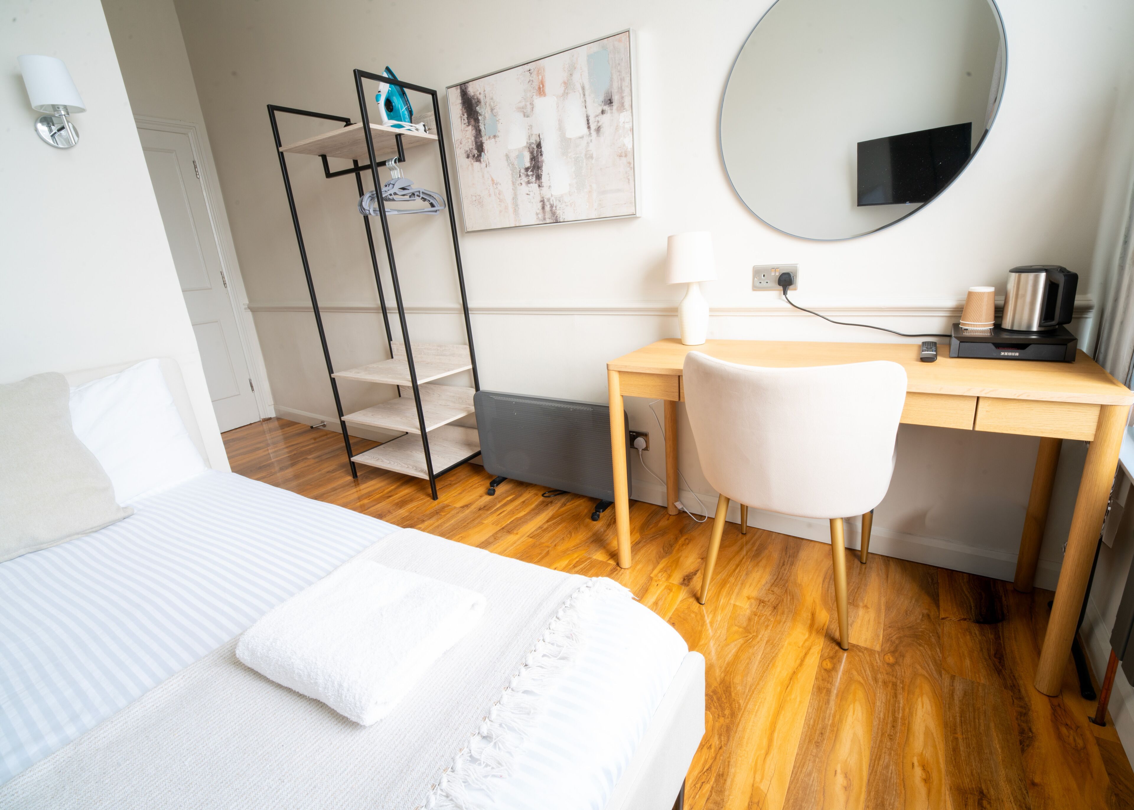 A hotel room with a bed, a desk, a chair, a wardrobe, a mirror, and a painting on the wall.
