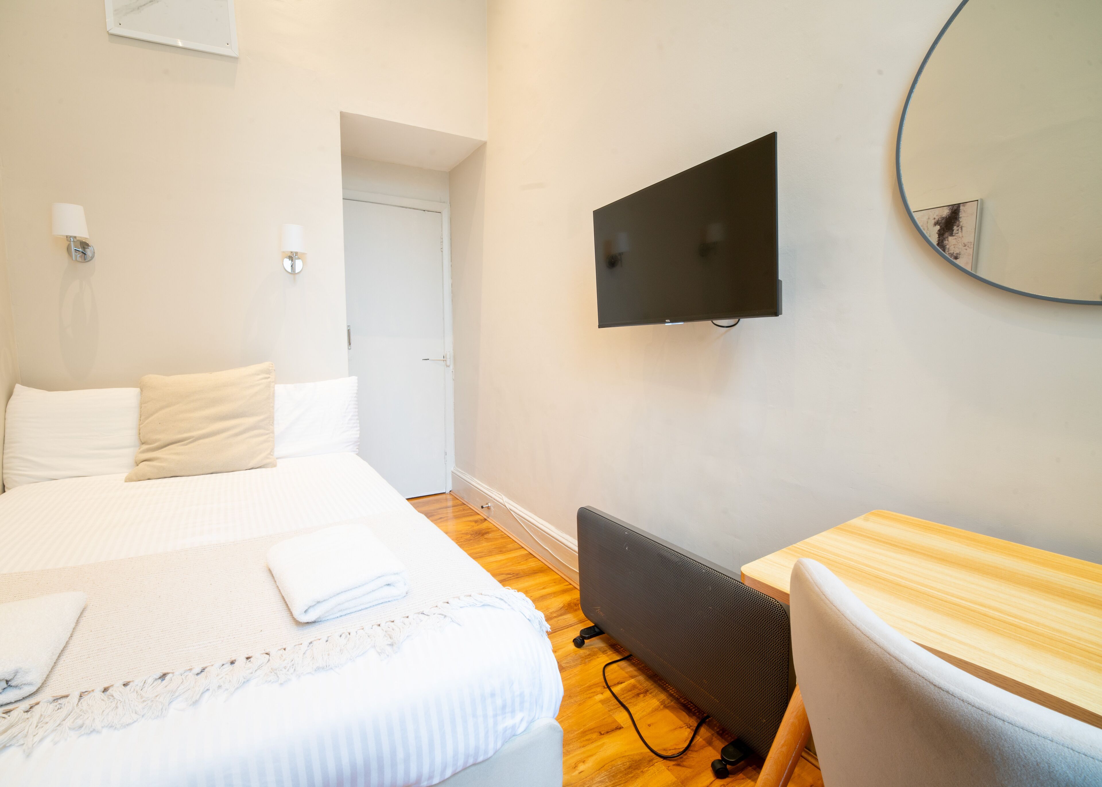 A bedroom with a bed, a desk, a TV, and a door.