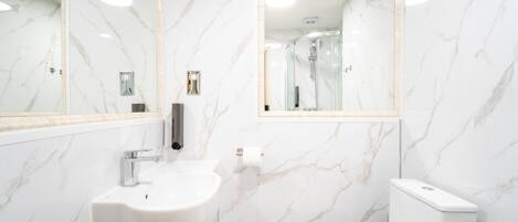 A bathroom with a white sink, mirror, and toilet against marble walls.