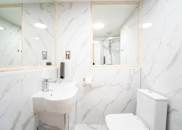 A bathroom with a white sink, mirror, and toilet against marble walls. - Rushmore Hotel (London)