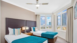 A hotel room with two beds, a ceiling fan, a nightstand, a lamp, and a window with a city view. - BreakFree Moroccan (Surfers Paradise)