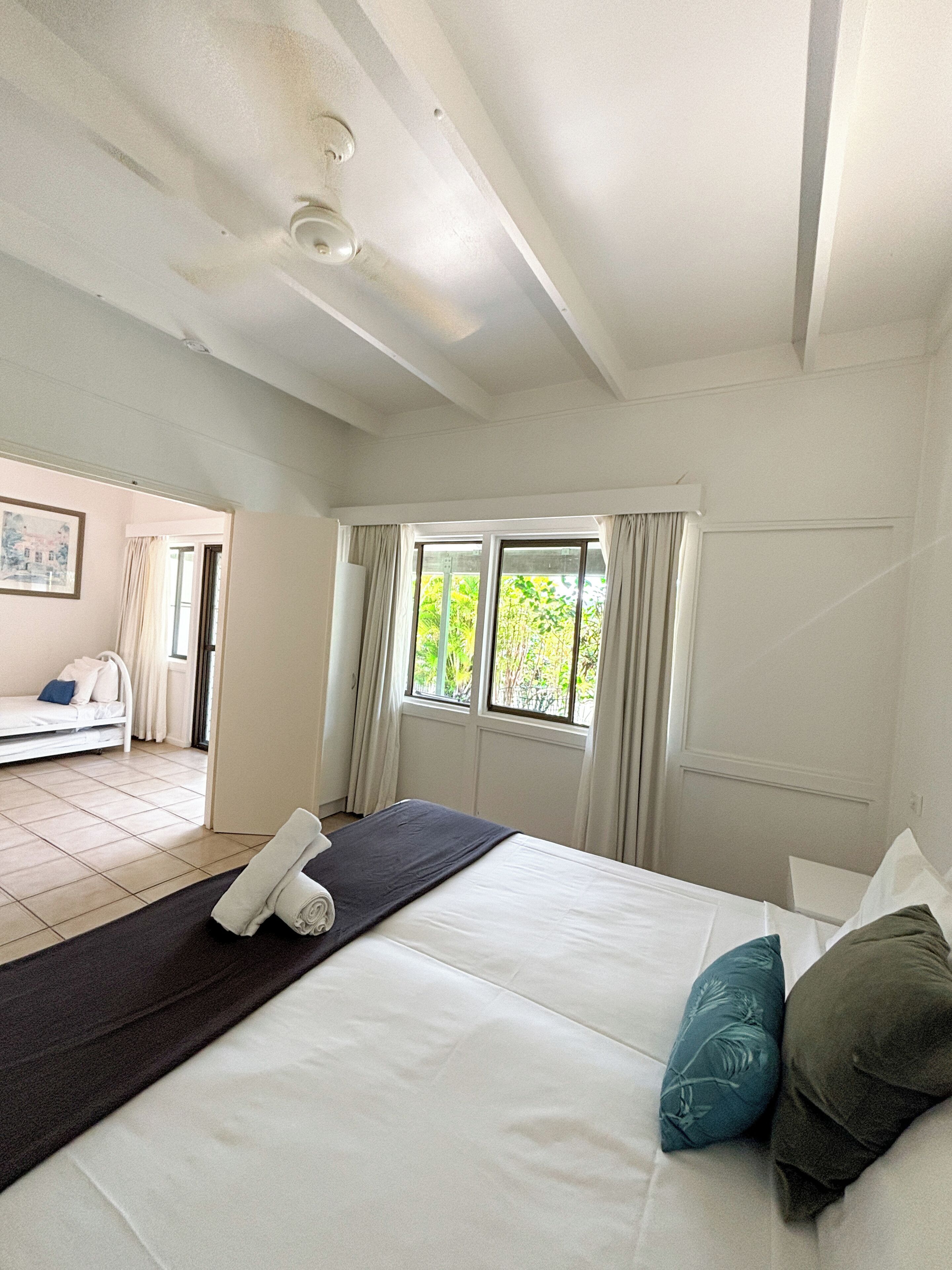 Un dormitorio con cama, ventana con cortinas, ventilador de techo y vista a un balcón.