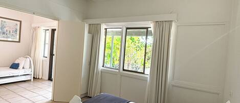 Un dormitorio con cama, ventana con cortinas, ventilador de techo y vista a un balcón.