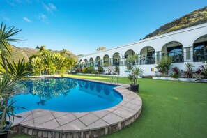A swimming pool with a tiled deck, surrounded by a well-maintained lawn and potted plants.