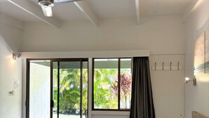 A bedroom with a bed, a ceiling fan, a window with curtains, and a view of greenery outside. - Amaroo Rainforest Resort (Nelly Bay)