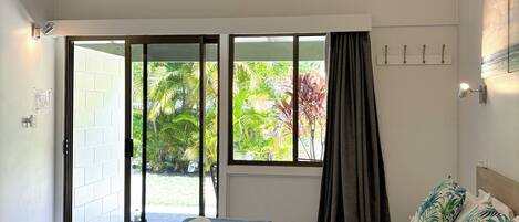 Une chambre à coucher avec un lit, un ventilateur de plafond, une fenêtre avec des rideaux et une vue sur la verdure à l’extérieur.