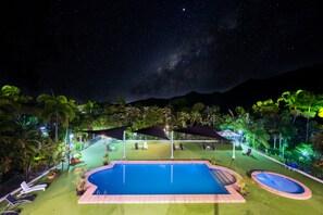 A nighttime view of a pool area with a clear sky, stars, and a mountain in the background.