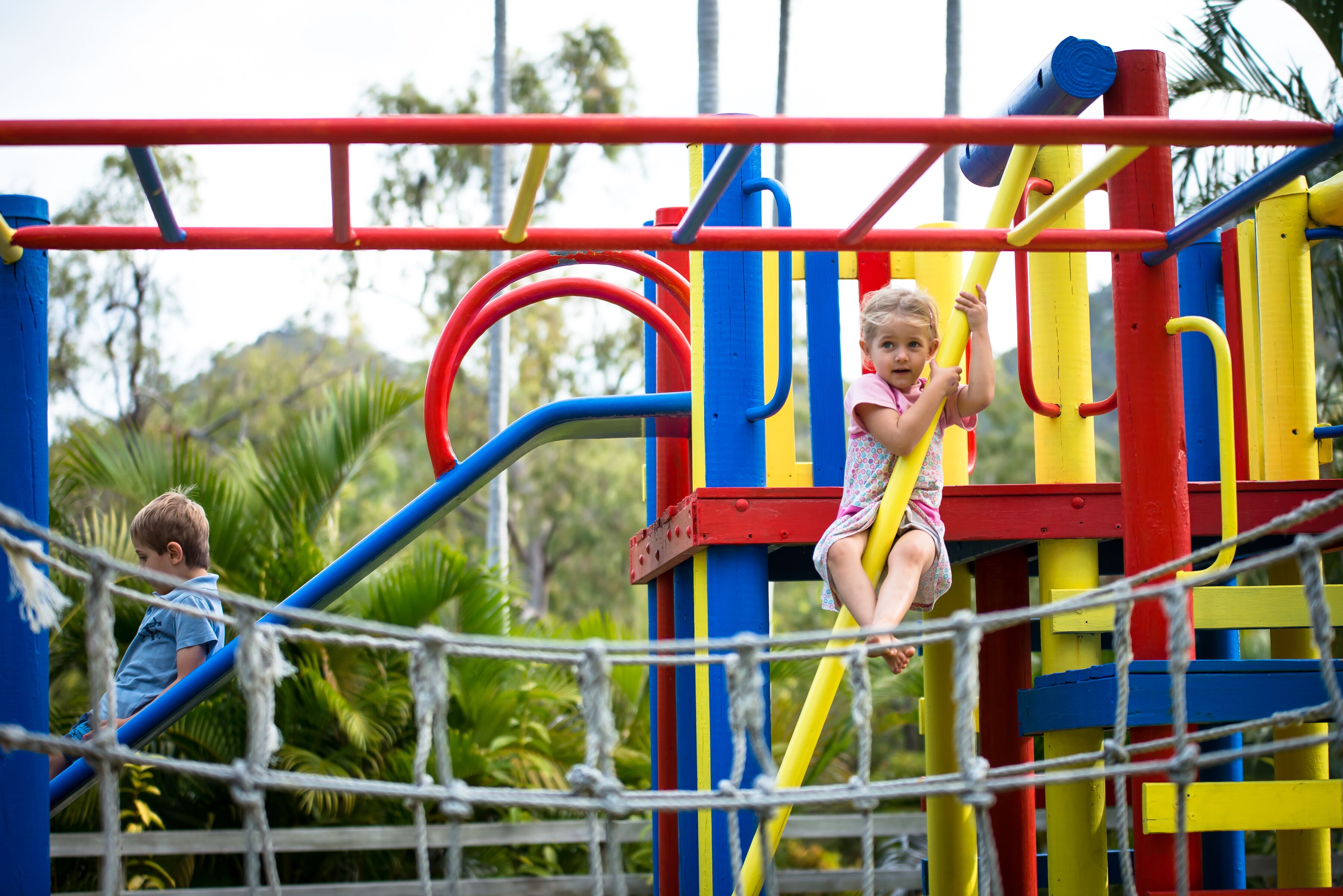 Children playing on a colorful playground structure with various climbing and hanging elements.