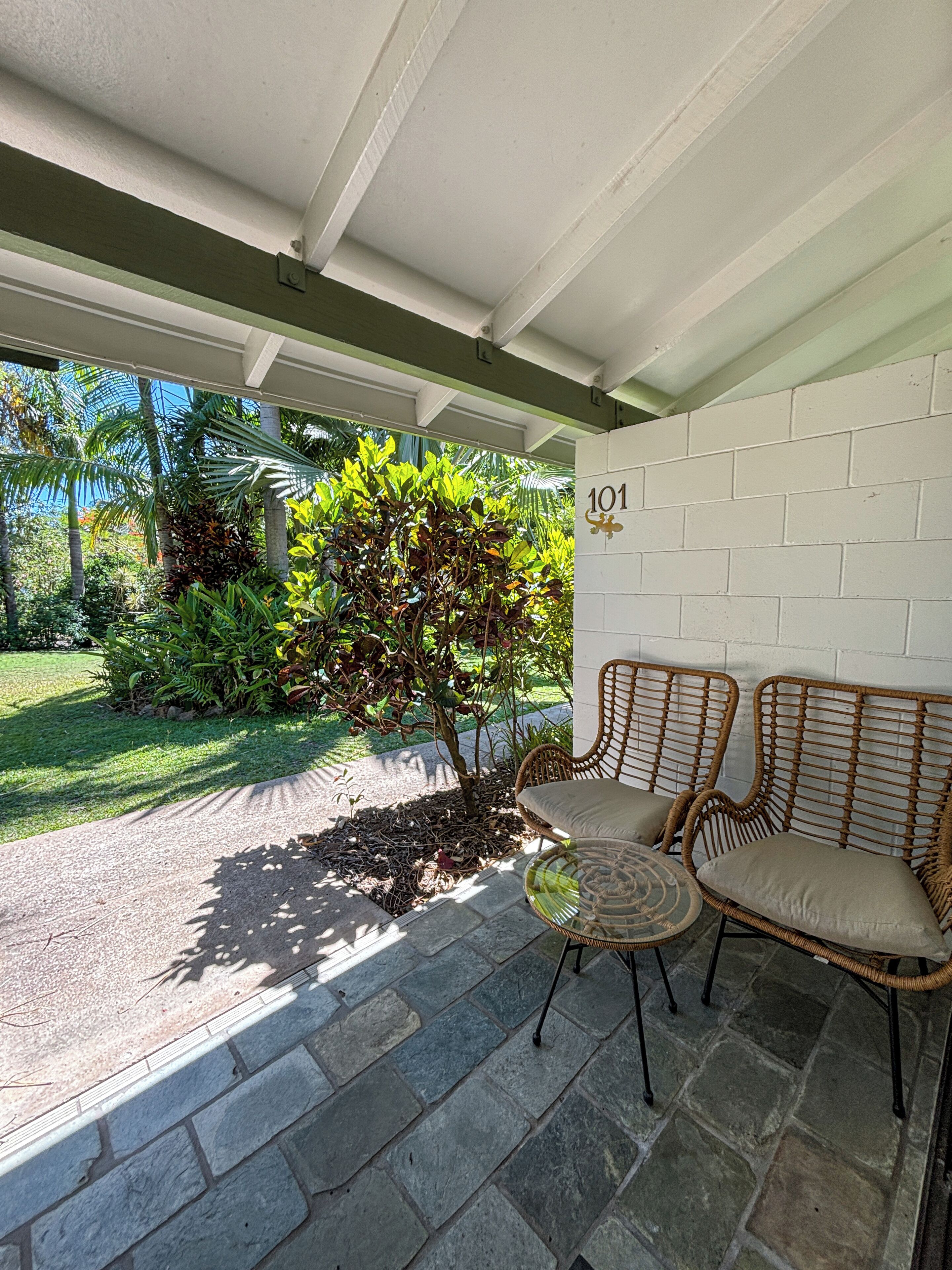 A covered patio area with a stone floor, two wicker chairs, a small table, and a potted plant.