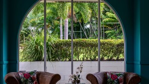 A room with two wicker chairs facing a large arched window overlooking a garden. - Amaroo Rainforest Resort (Nelly Bay)