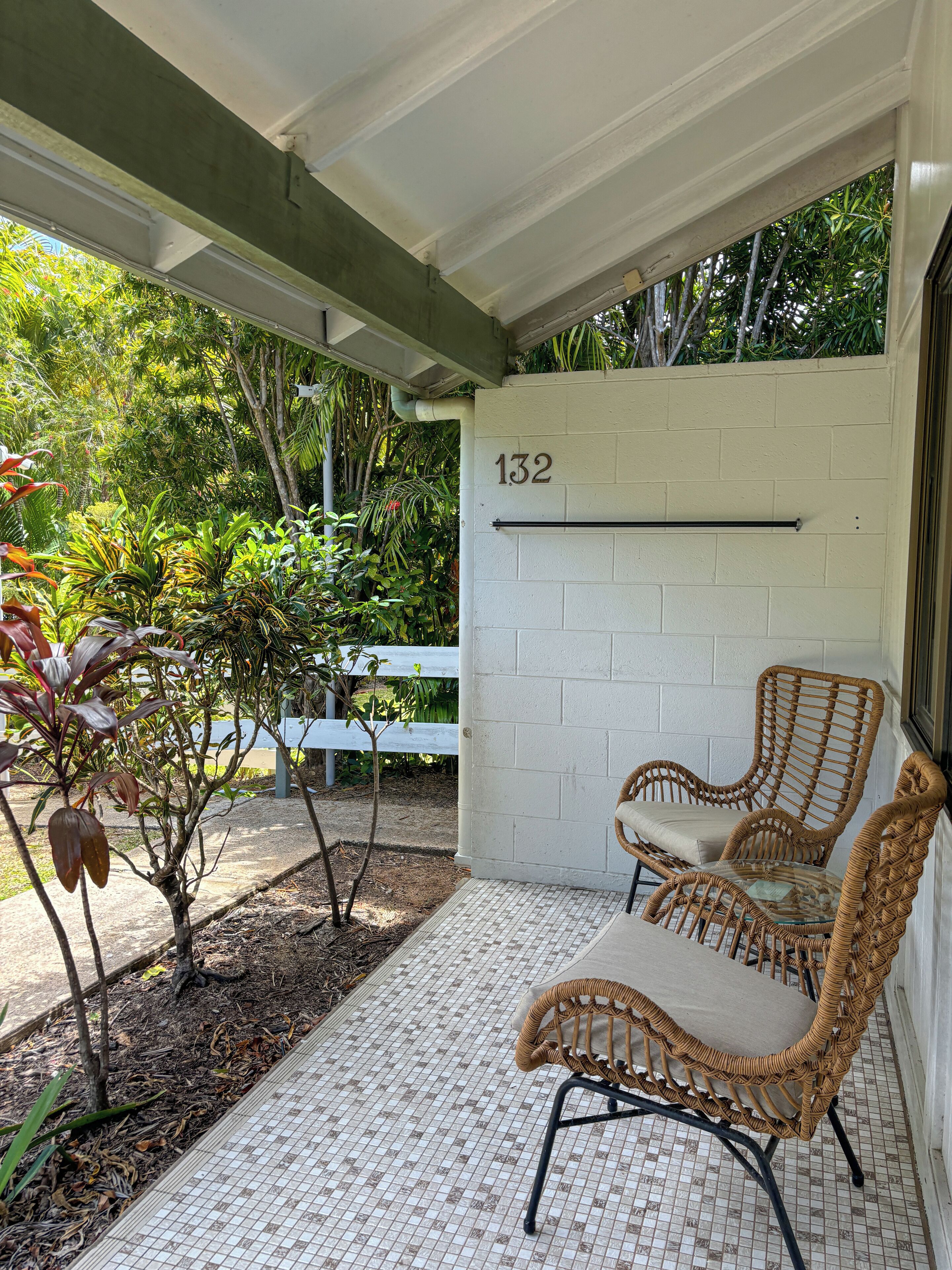 A covered outdoor seating area with wicker chairs and a white wall with the number 132.