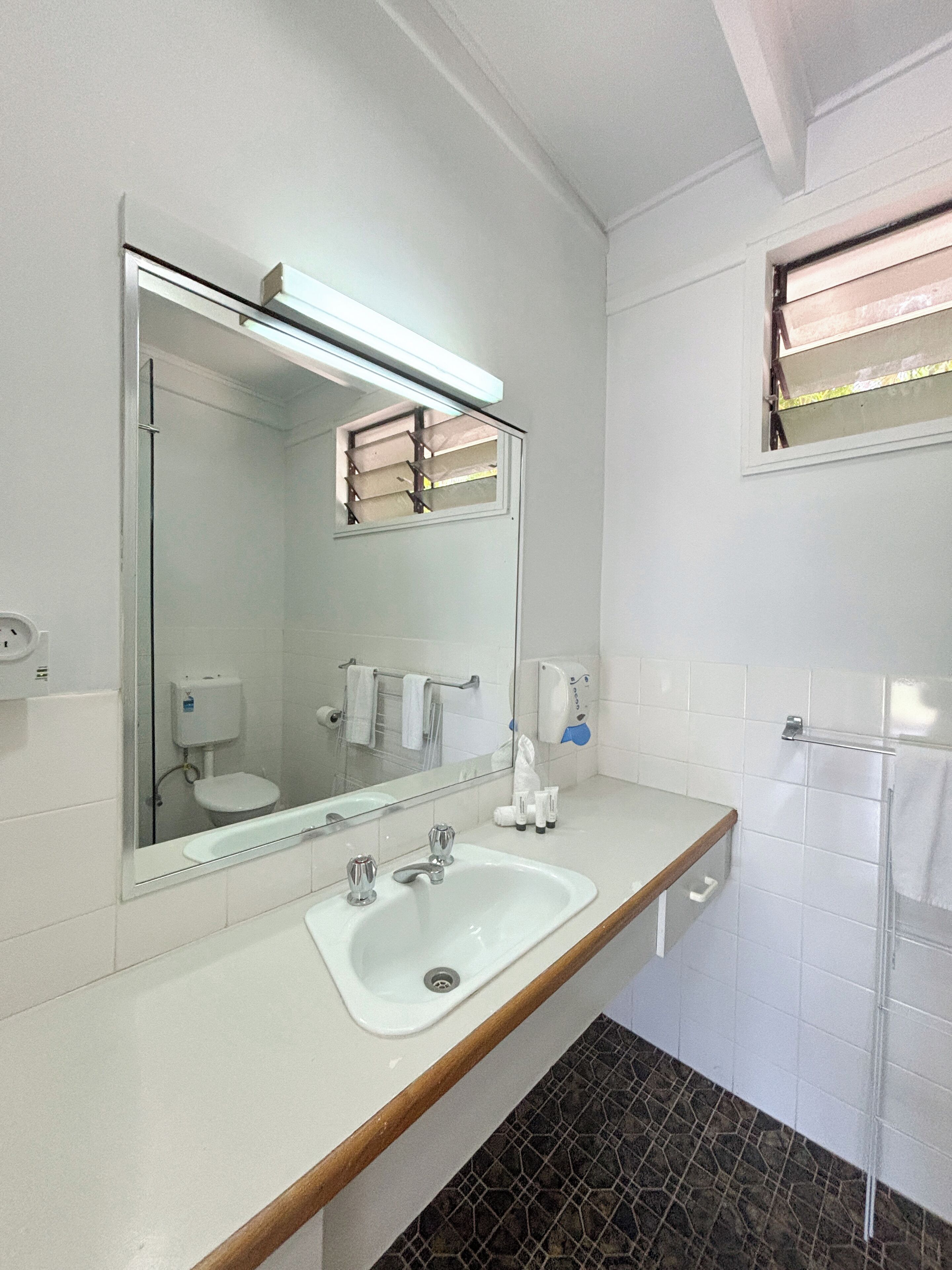 Un baño con lavamanos blanco, espejo, ducha e inodoro.