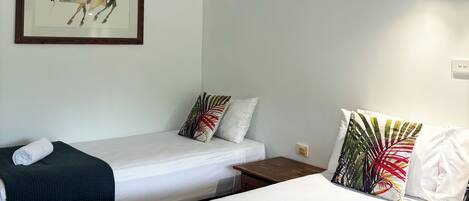 Habitación de hotel con dos camas individuales, un ventilador de techo, una obra de arte enmarcada de un caballo y una lámpara fijada a la pared.