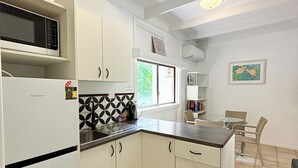 A compact kitchen with white cabinets, a black and white tiled backsplash, a microwave, and a small dining area with wicker chairs. - Amaroo Rainforest Resort (Nelly Bay)