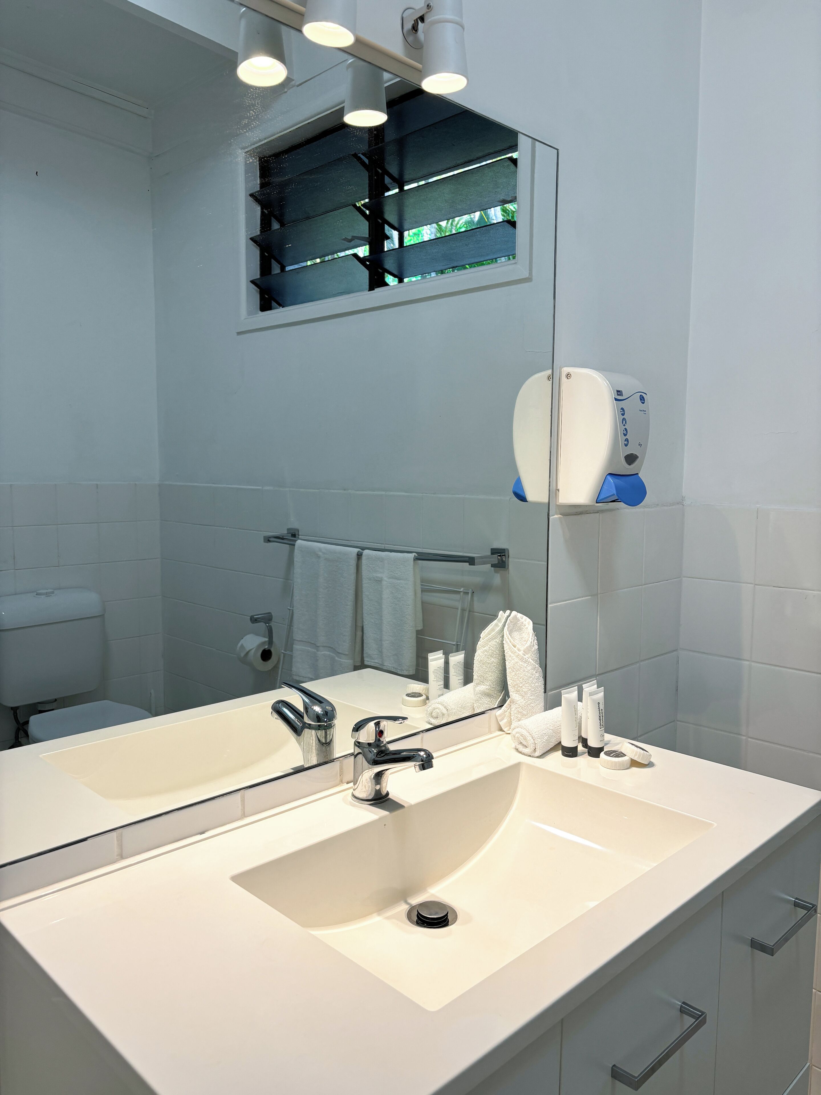 A modern bathroom with a large mirror, a sink, and a hand soap dispenser.