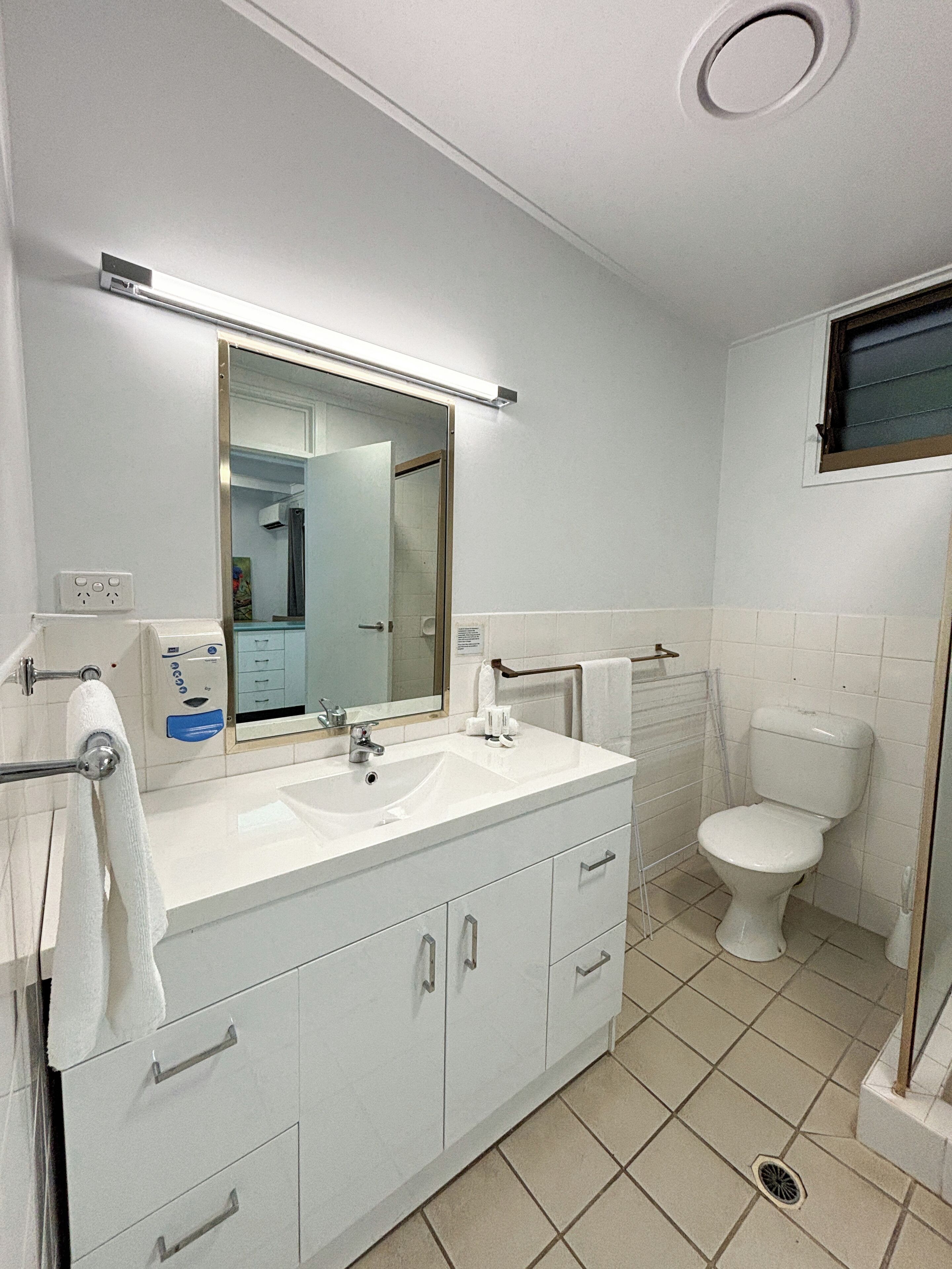 A modern bathroom with a white sink, mirror, and toilet. There is a towel rack and a shower area visible.