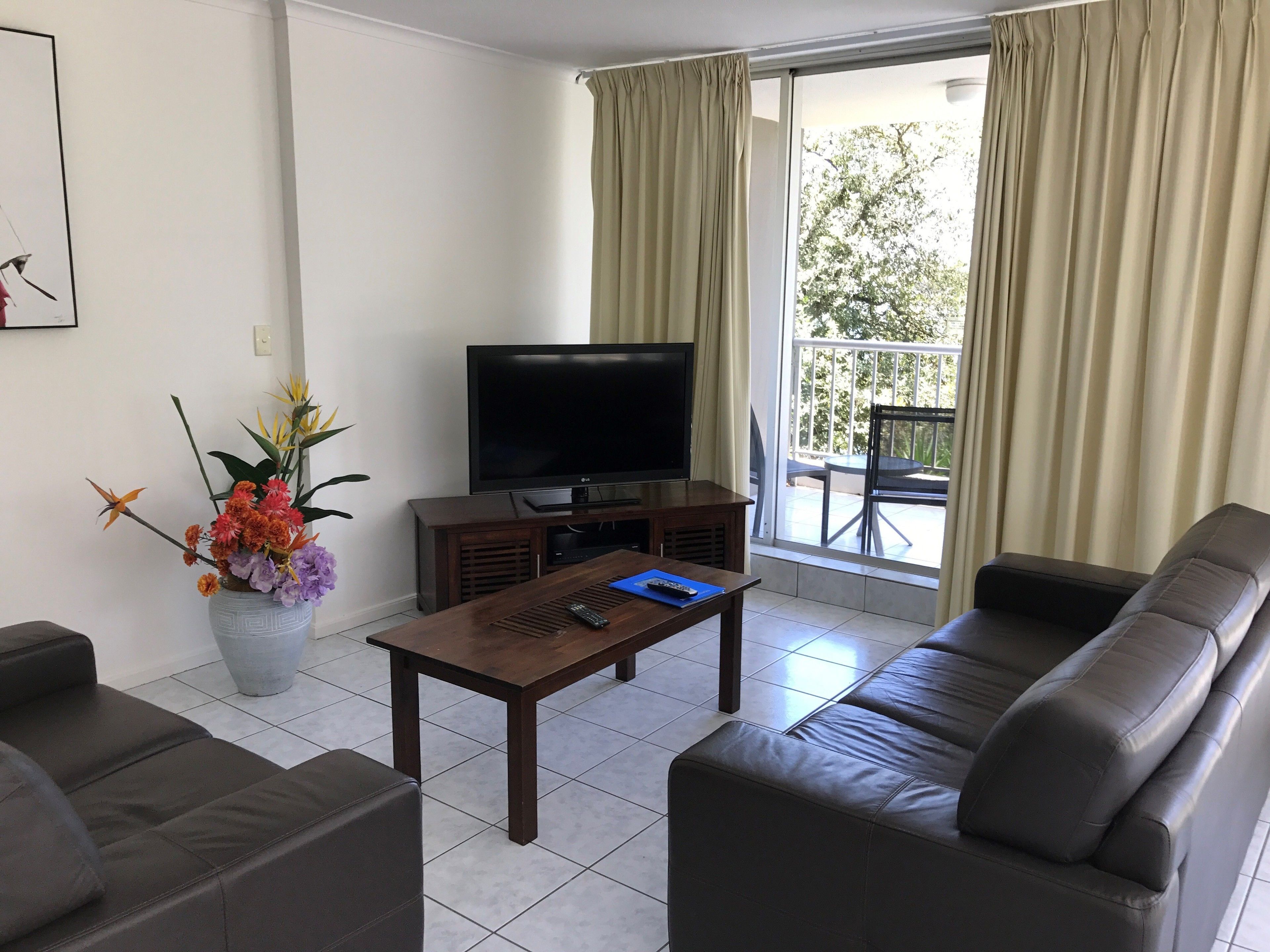 Una sala de estar con sofá, una mesa de centro, televisor y un balcón con cortinas.