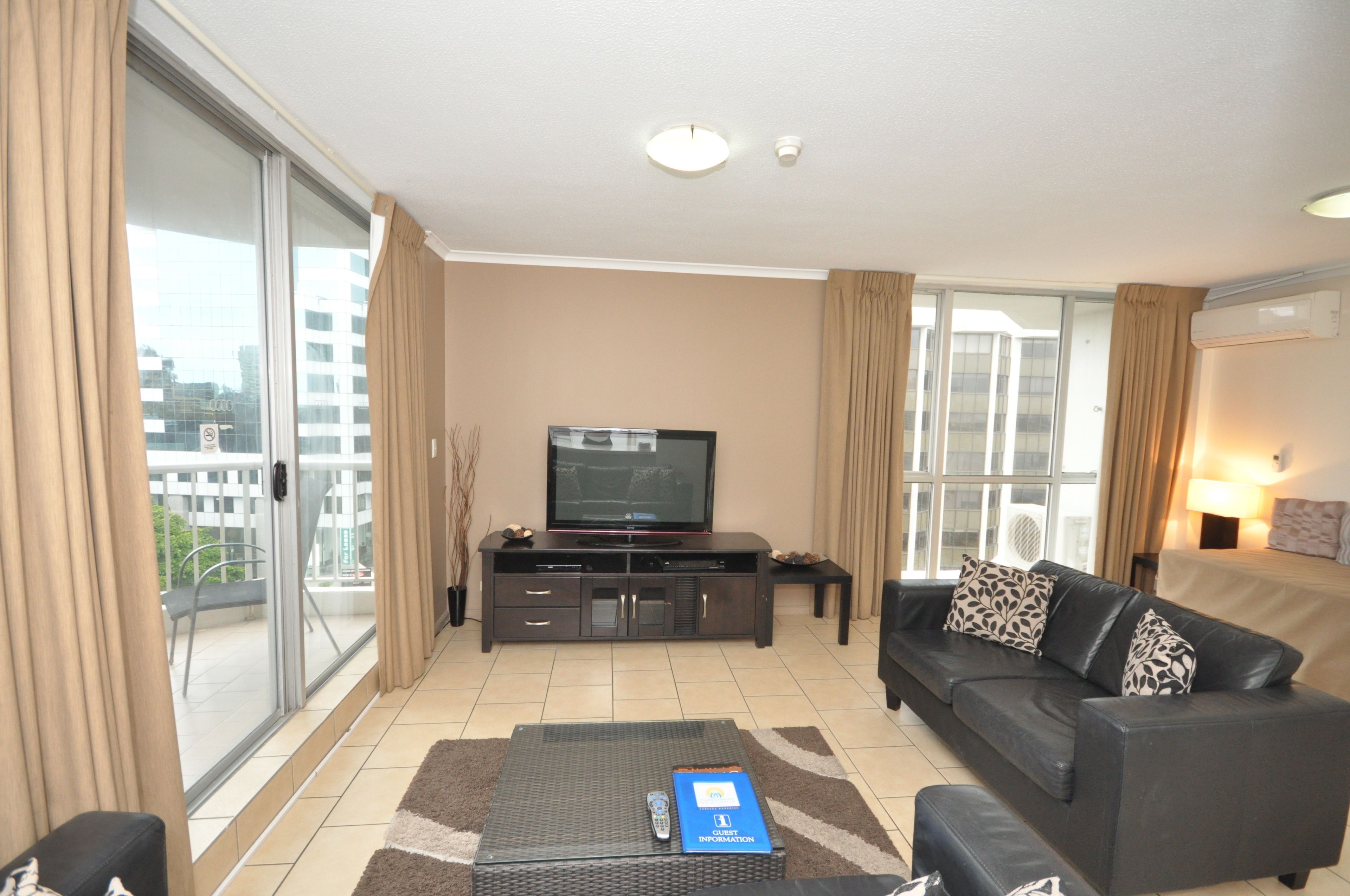 A modern living room with a flat-screen TV, a sofa, a coffee table, and a sliding glass door to the outside.
