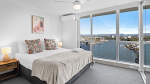Habitación de hotel con una cama grande, vistas al agua y al paisaje urbano, un ventilador de techo y un cuadro en la pared.