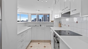 Una cocina moderna con armarios blancos, un ventanal con vista a la ciudad y piso de baldosas.