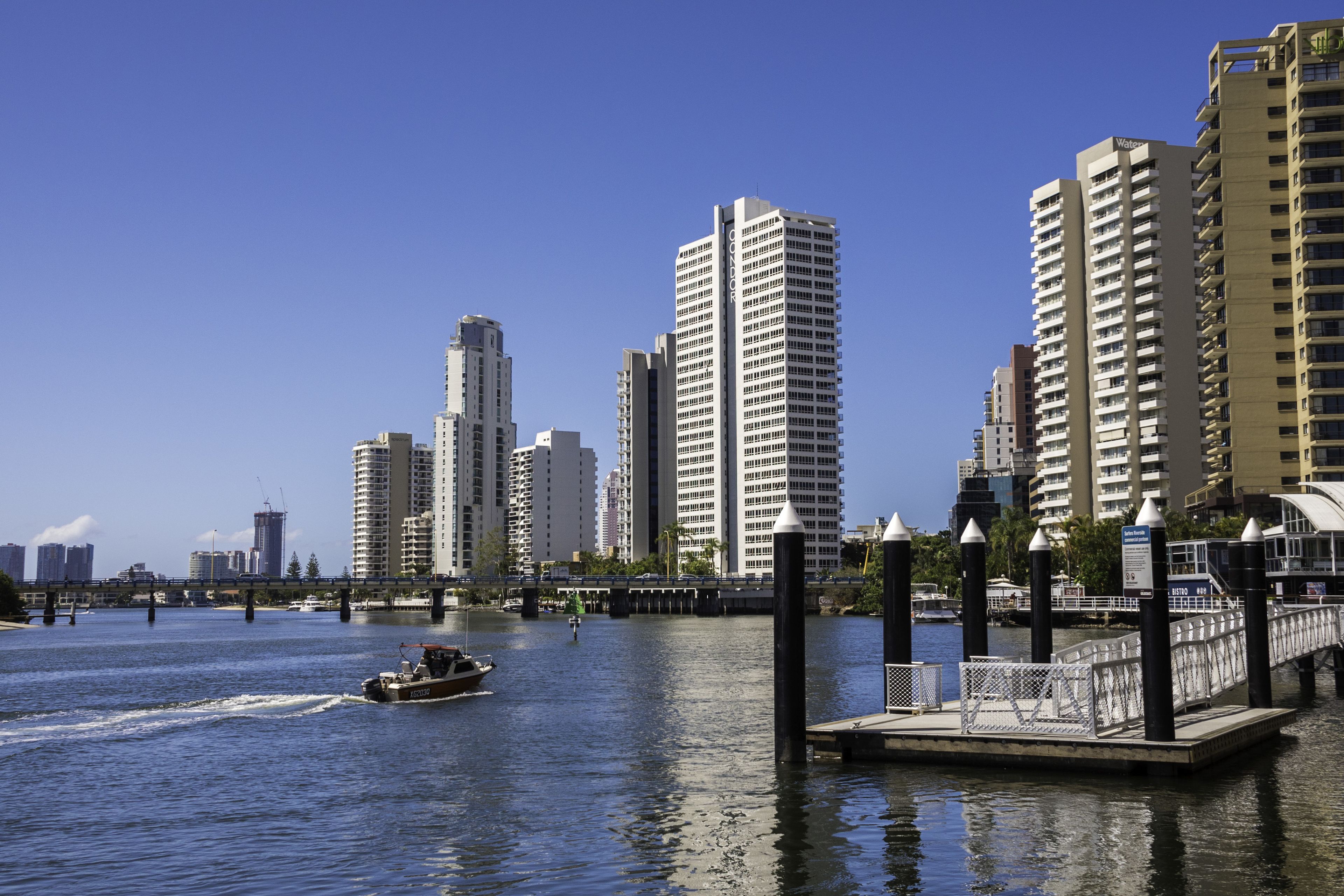 A waterfront cityscape with high-rise buildings, a bridge, and a boat on the water.