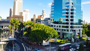 Un moderno edificio de gran altura con fachada de vidrio, rodeado de palmeras y otras construcciones urbanas.