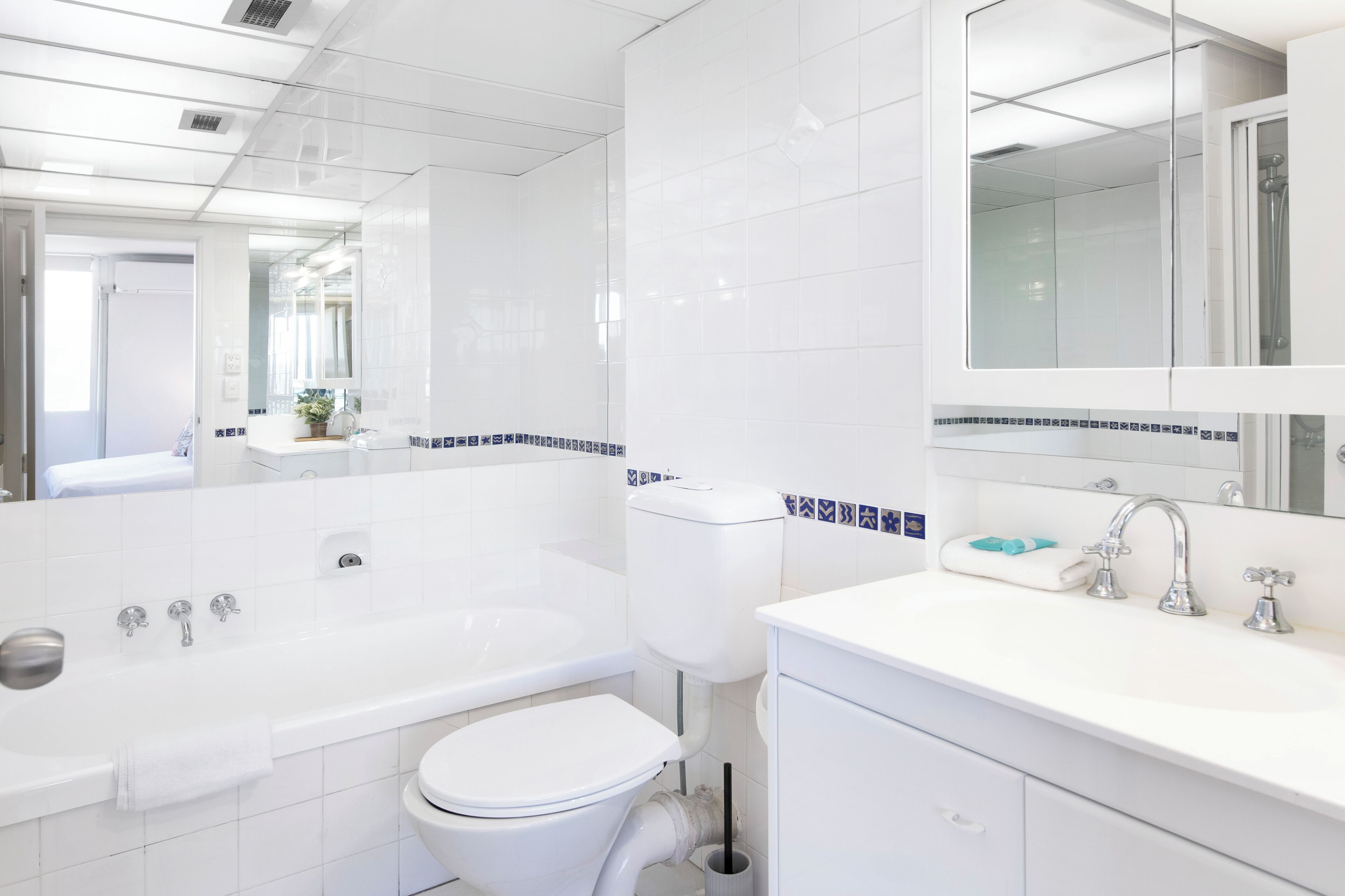 Un baño moderno con bañera, inodoro y lavamanos, con azulejos blancos y un espejo grande.