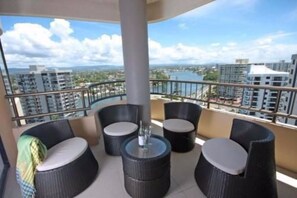 A balcony with wicker furniture and a view of a cityscape and water. - The Regent Apartments (Surfers Paradise)