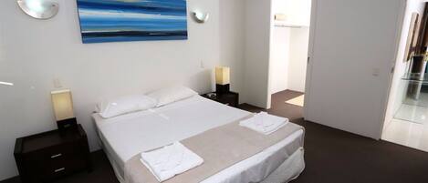 A modern hotel room with a large bed, two bedside tables with lamps, a painting on the wall, and a glass door leading to a balcony.