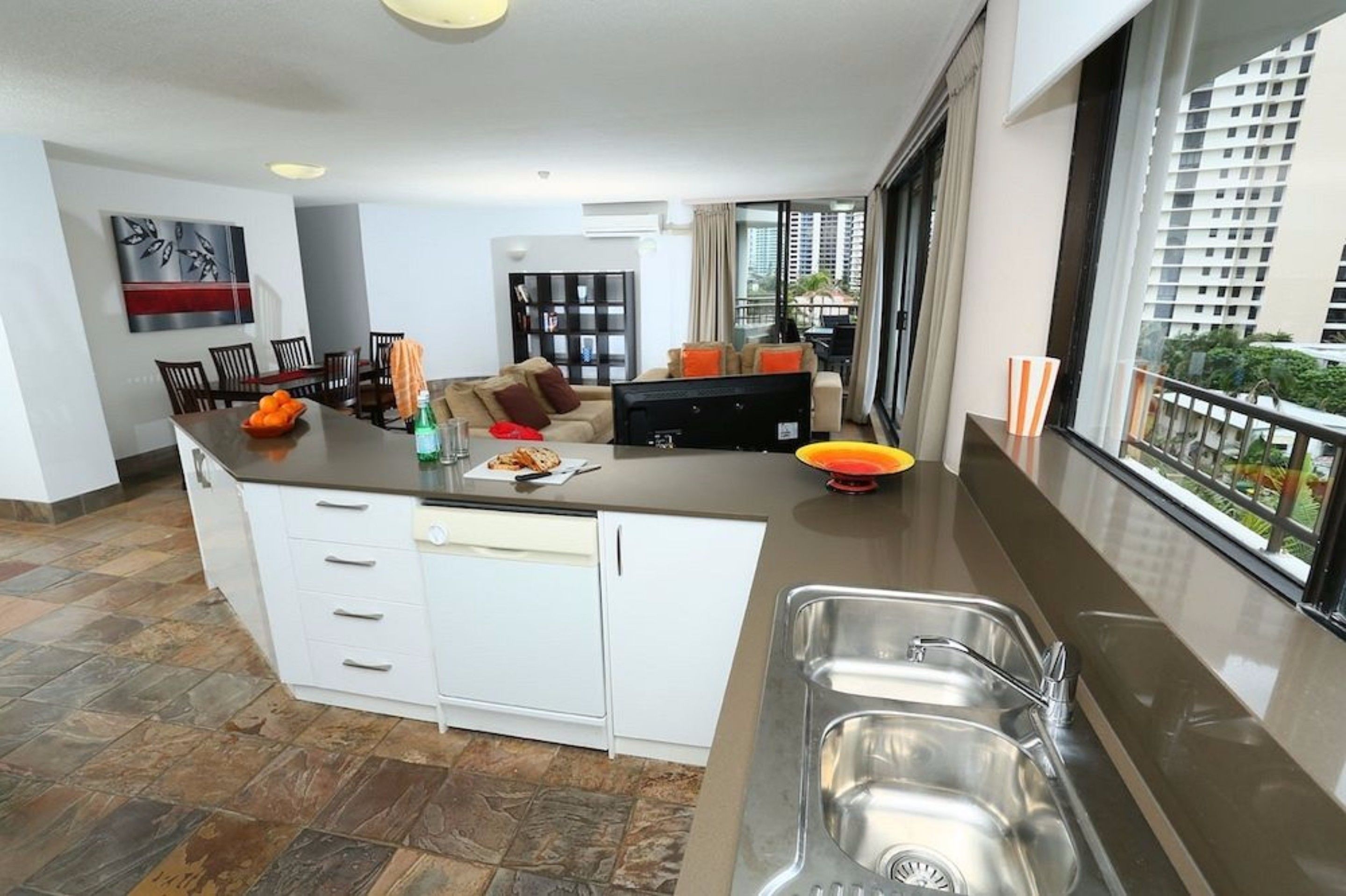 Une cuisine moderne dotée d’un îlot central, d’un coin repas avec des chaises, d’un canapé et d’un téléviseur.