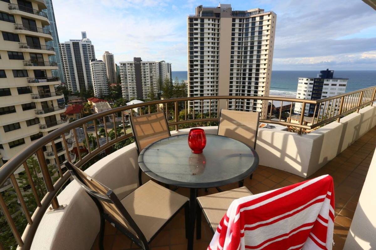 A balcony with a round table, chairs, and a red vase.
