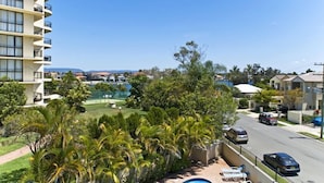 Un hotel moderno de altura con varios balcones, piscina y vistas a una zona residencial con casas y vegetación.