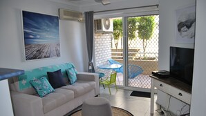 Un salón con sofá, reposapiés, televisor y vistas al exterior a través de un ventanal.