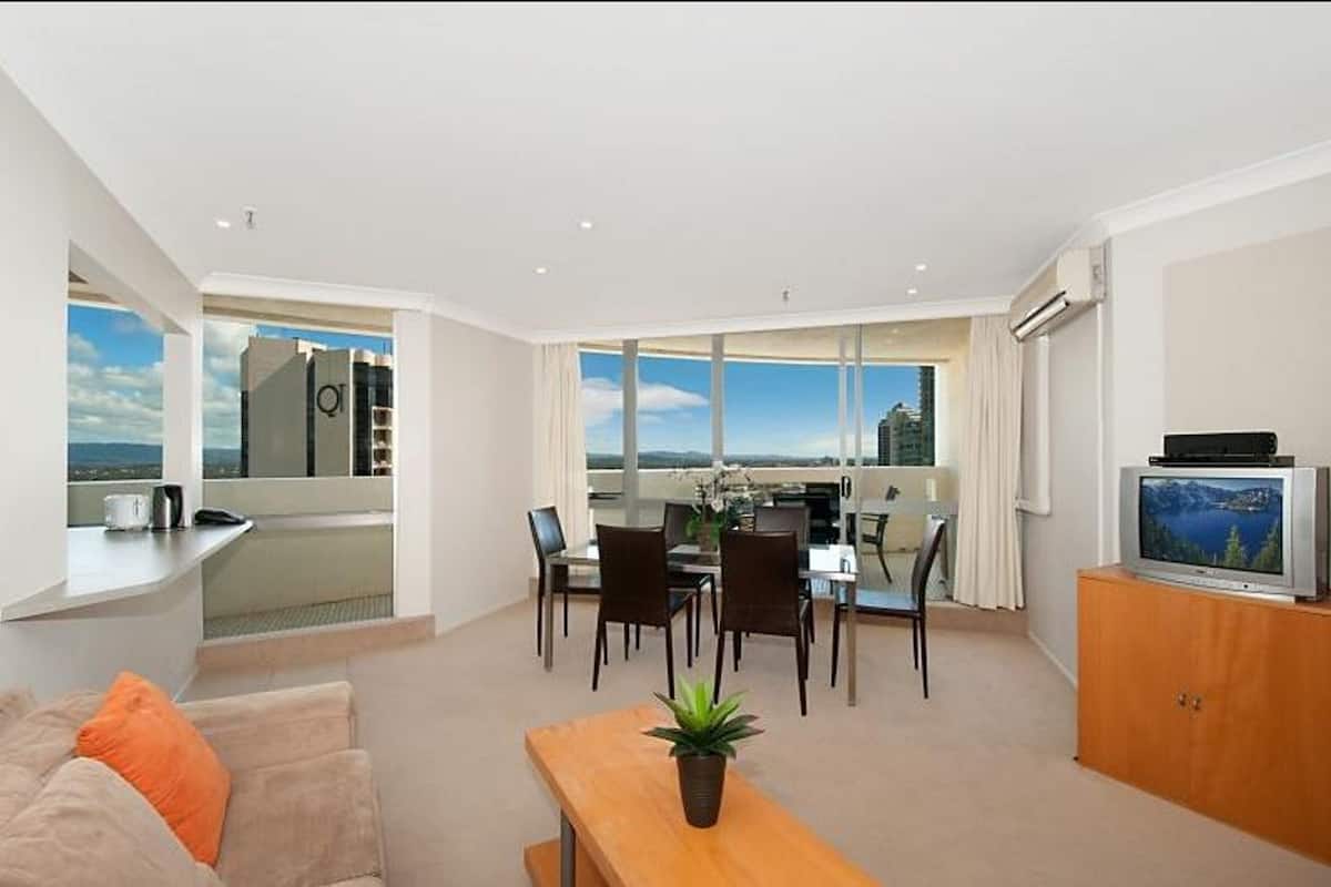 A modern living room with a dining area, a TV on a wooden cabinet, and a balcony with a city view.