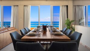 Un área de comedor con vista al océano, una mesa de madera dispuesta para cuatro personas y un sofá con vistas.